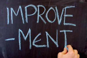 A hand writing the word improvement on a chalk board